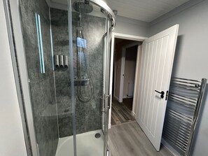 A modern bathroom with a glass-enclosed shower, a white bathtub, and a door leading to another room. - 2bedroom-1bathroom-patio-wifi (Auchterarder)