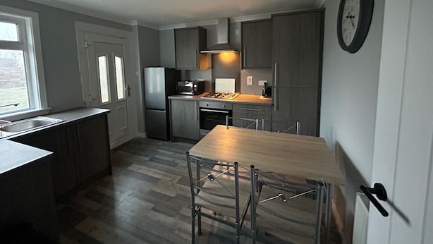 A compact kitchen with a central island, a sink, and a dining area with chairs. - 2bedroom-1bathroom-patio-wifi (Auchterarder)