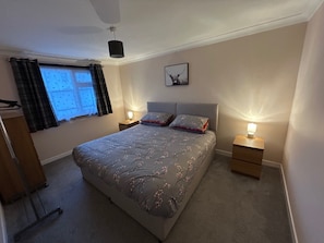 A bedroom with a large bed, two bedside tables with lamps, a window with curtains, and a wall-mounted picture. - 2bedroom-1bathroom-patio-wifi (Auchterarder)