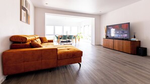 Een moderne woonkamer met een grote bank, een flatscreen televisie en een houten kast.
