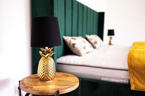 A bed with a green headboard, a round wooden nightstand with a lamp, and a yellow throw blanket. - Stylish apartment in downtown Andernach with a view, Wi-Fi, kitchen, and parking (Andernach)