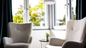 Twee fauteuils gericht op een raam met uitzicht op bomen en een kleine tafel met een plant.