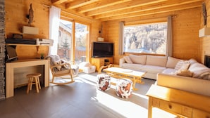 A wooden cabin interior with a sofa, TV, wooden desk, and a view of a snowy landscape. - La Tanière : Exceptional Alpine chalet with heated pool & sauna - 14 pers (Vars)