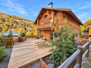 Een houten chalet met een balkon, terras en uitzicht op een bebost gebergte.