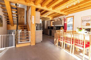 Une cuisine spacieuse équipée d’appareils modernes, un coin repas avec des chaises et une table en bois, et un escalier menant à l’étage supérieur.