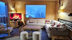A cozy cabin interior with a fireplace, a sofa, ottomans, and a wooden chest. - La Tanière : Exceptional Alpine chalet with heated pool & sauna - 14 pers (Vars)