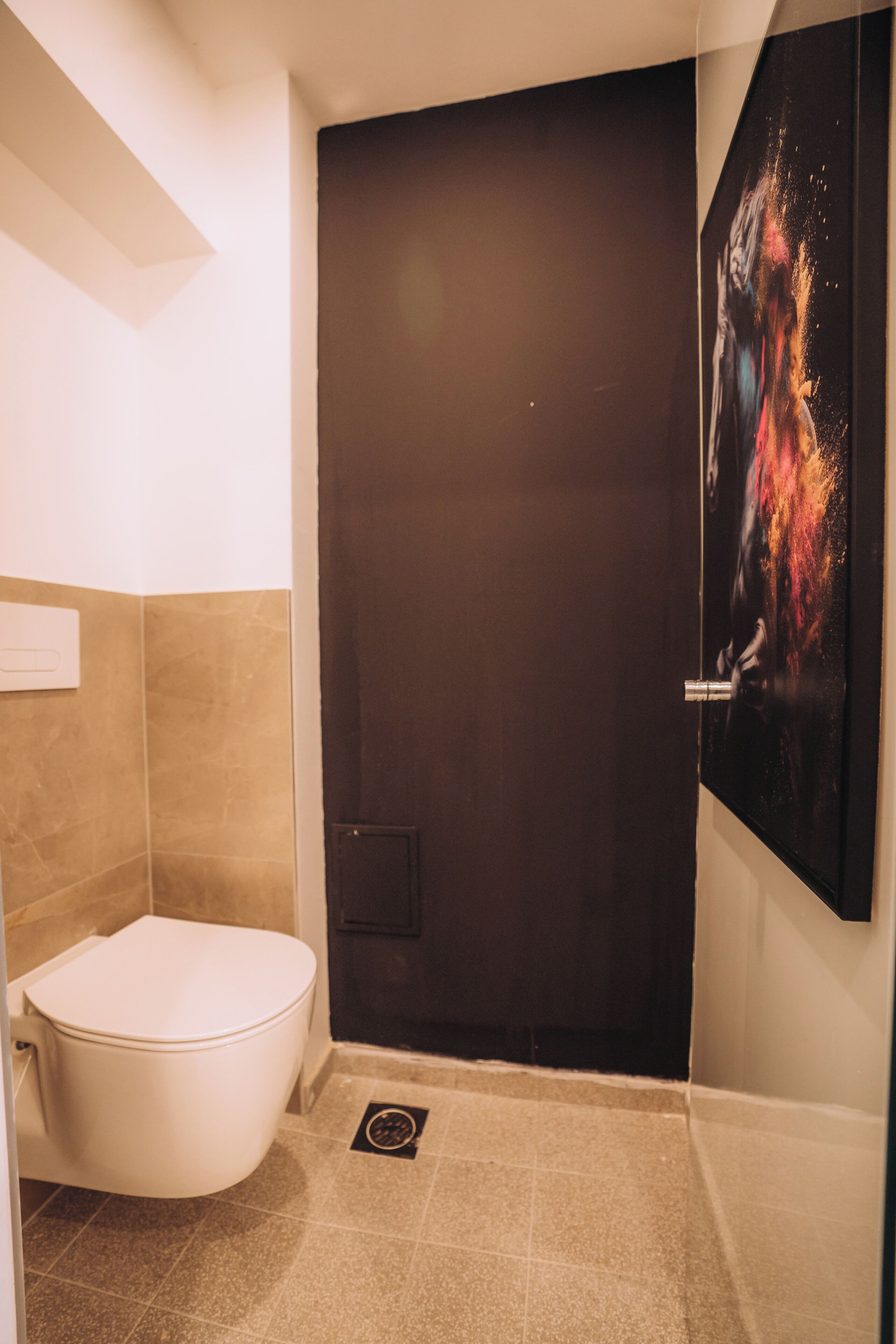Un bagno con il water bianco, una porta scura e un poster appeso al muro.