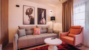 A modern living room with a grey sofa, a round coffee table, a red patterned rug, and a red armchair. There are two framed pictures on the wall and a floor lamp.