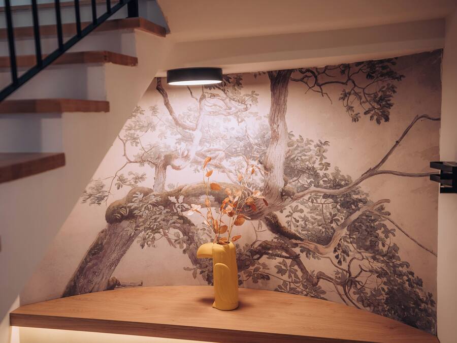 A wooden table with a vase of dried flowers, a staircase, and a wall mural.