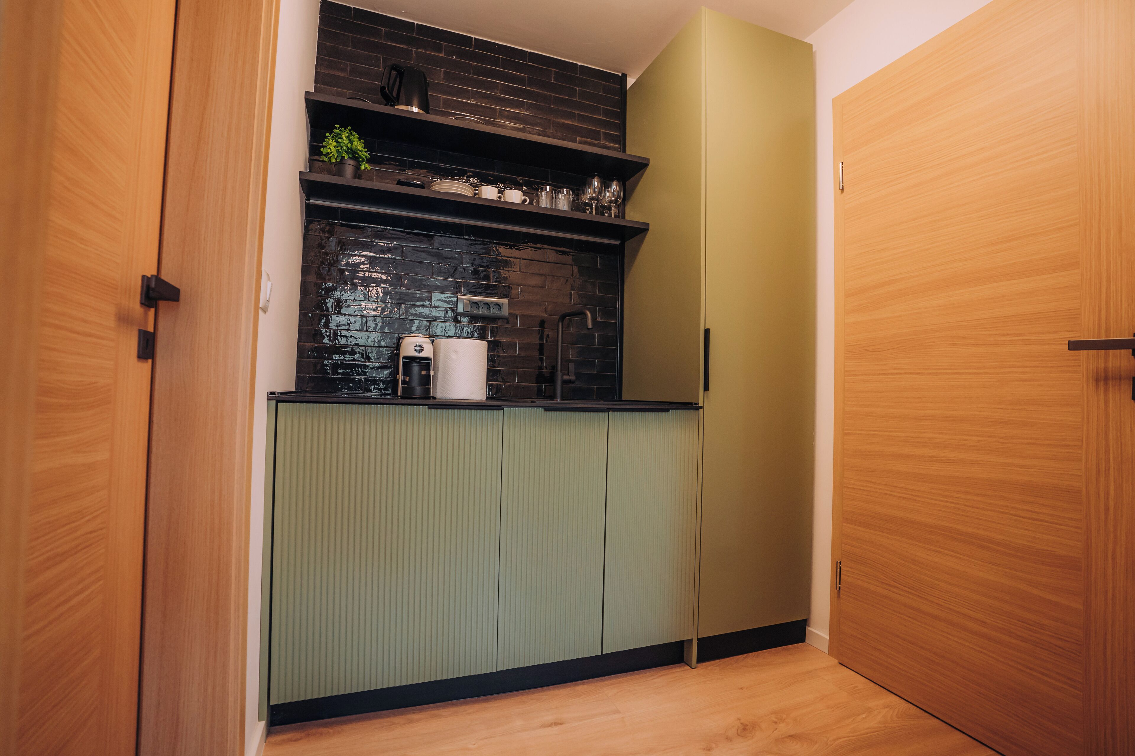 A compact kitchen with a black backsplash, green cabinets, and wooden doors.