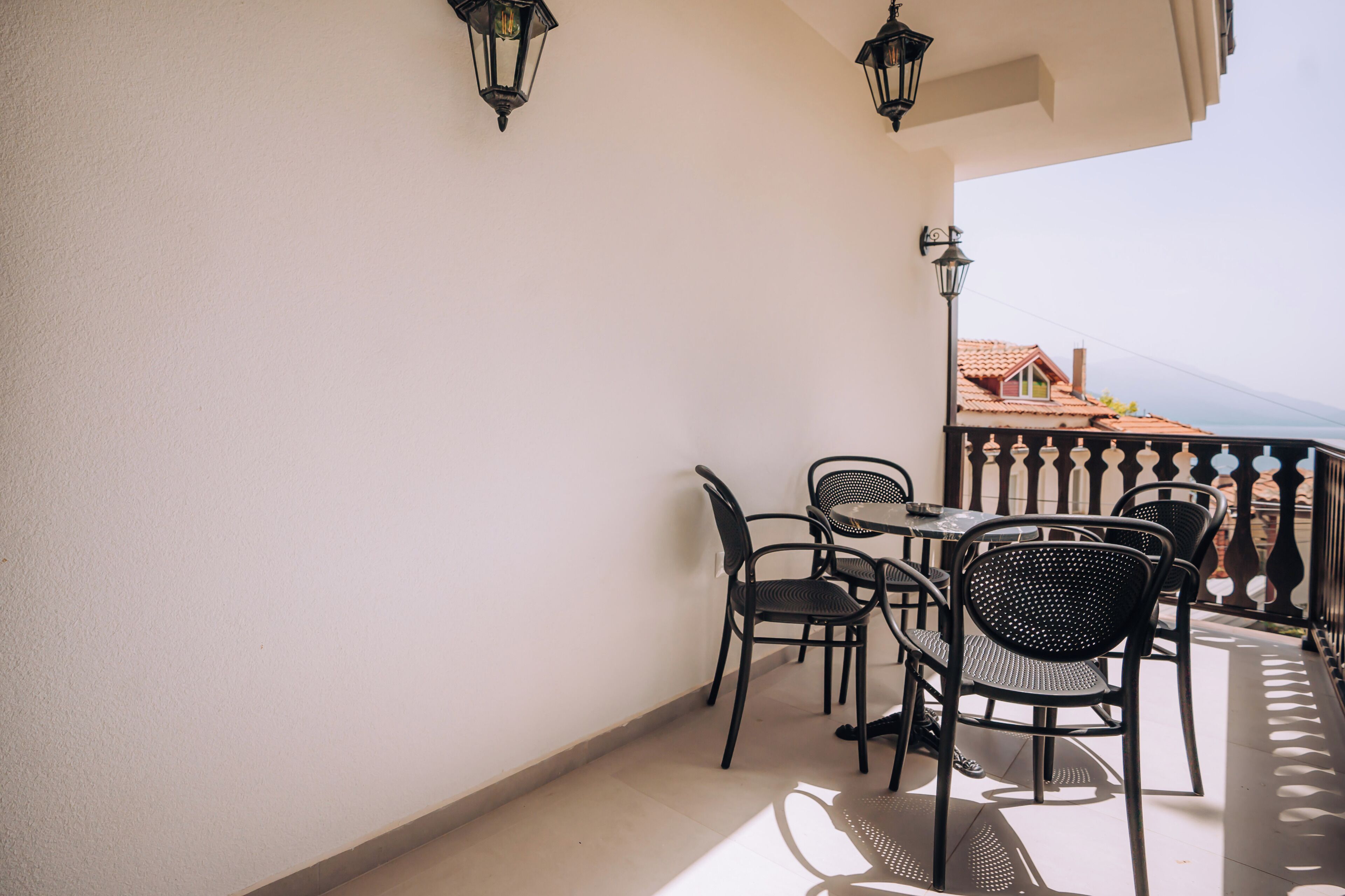A balcony with a table and chairs, a railing, and a view of a building with a red roof.