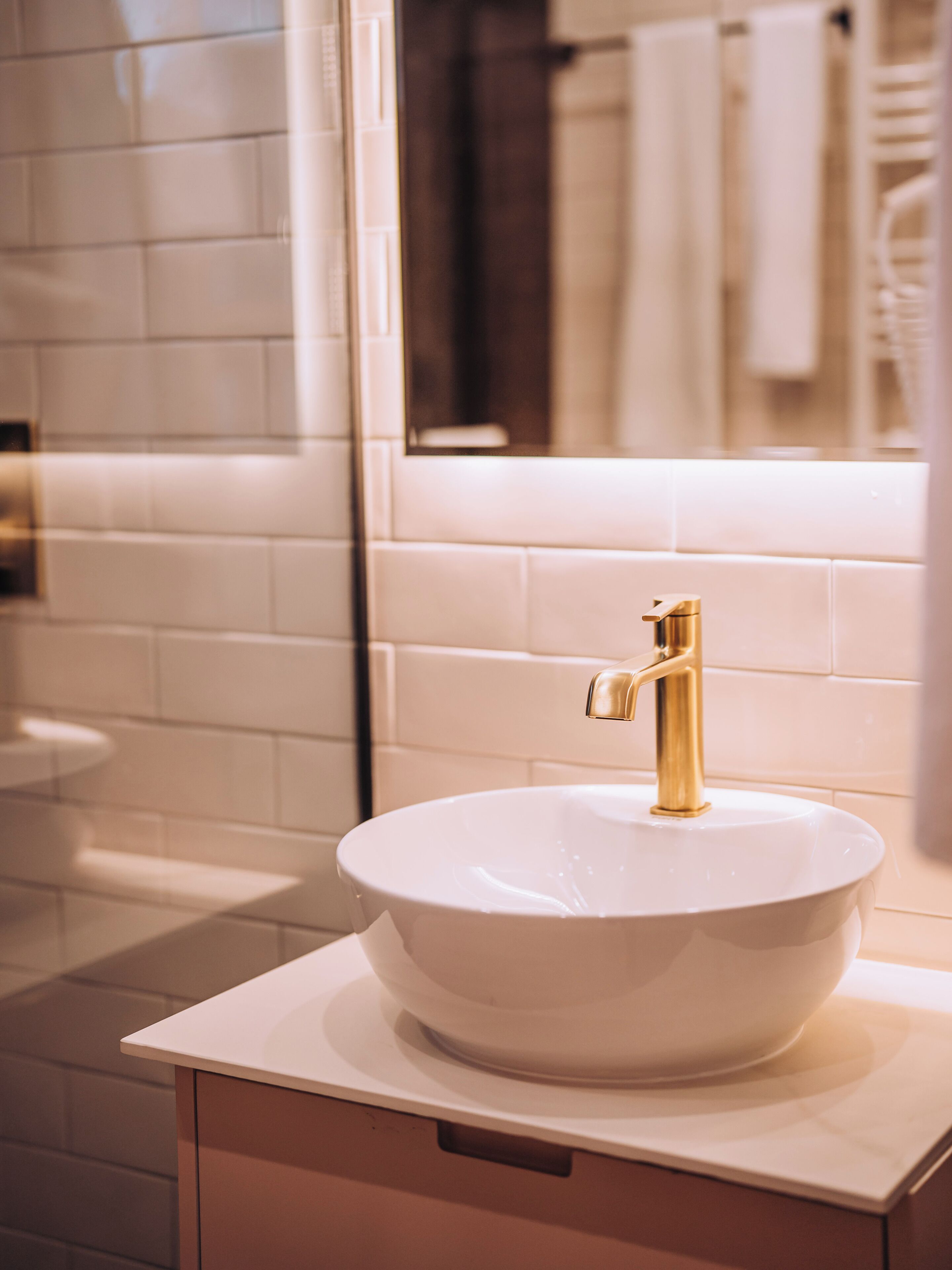 A bathroom with a white sink, gold faucet, and white tiles.