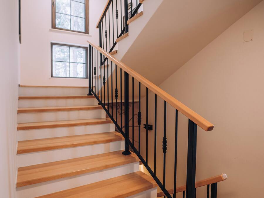 Una escalera de madera con barandillas negras y un pequeño ventanal en la parte superior.