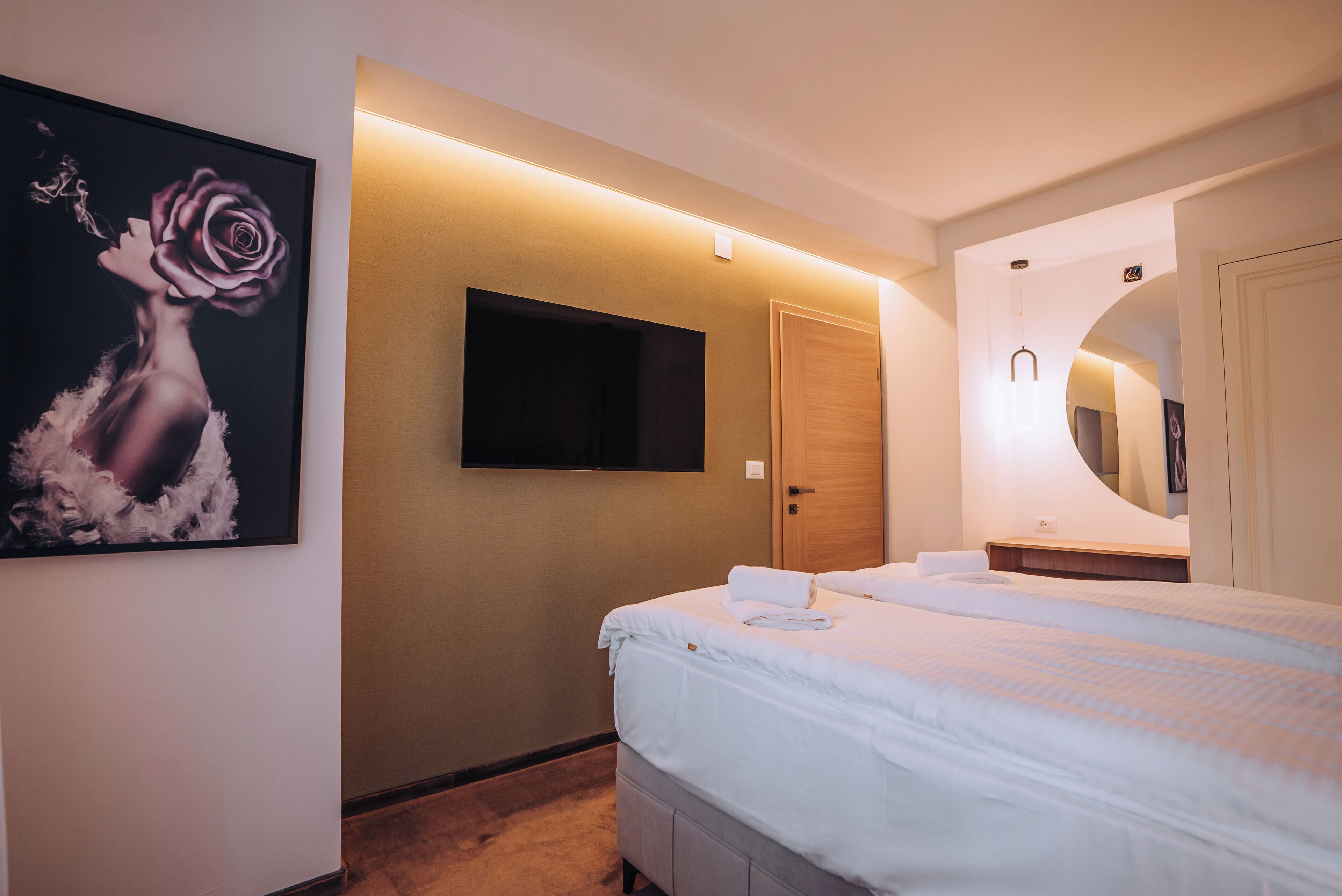A hotel room with a bed, a mounted TV, a painting, and a mirror.
