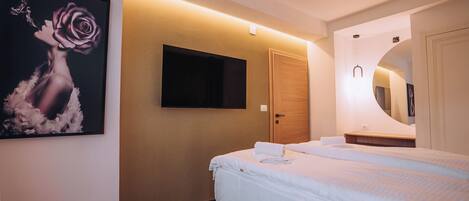 A hotel room with a bed, a mounted TV, a painting, and a mirror.