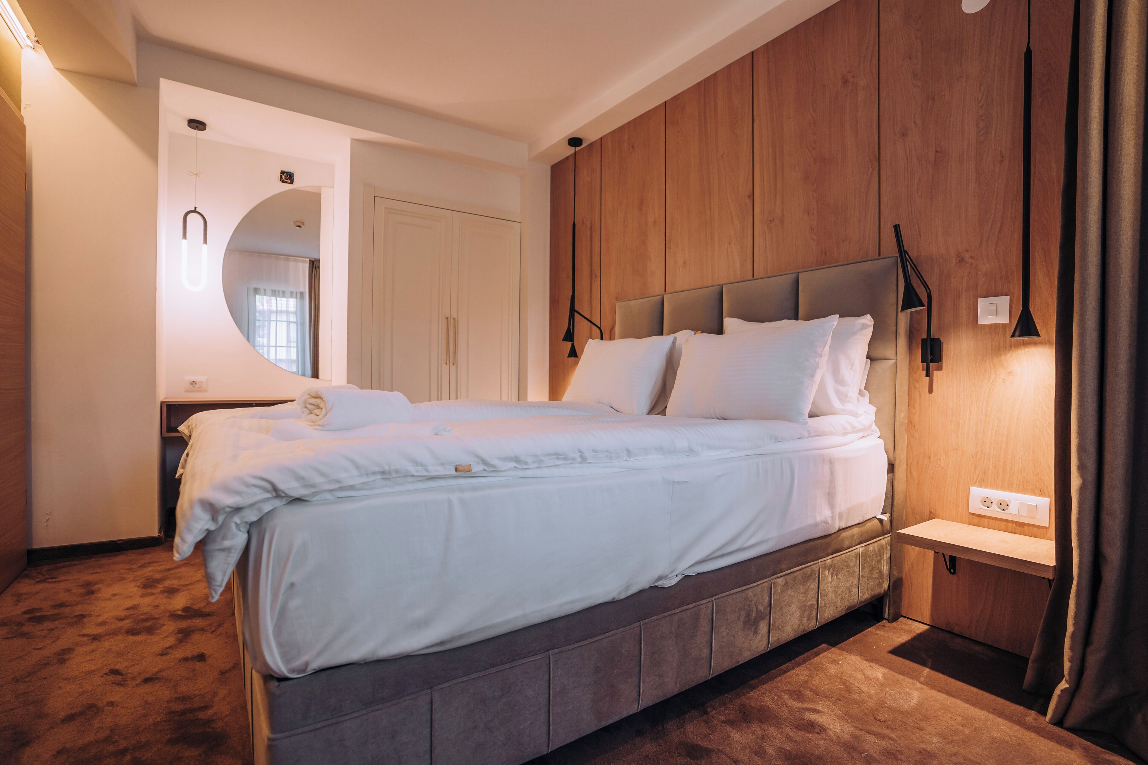 Un dormitorio moderno con una cama grande, paneles de madera, un banco empotrado y un espejo.