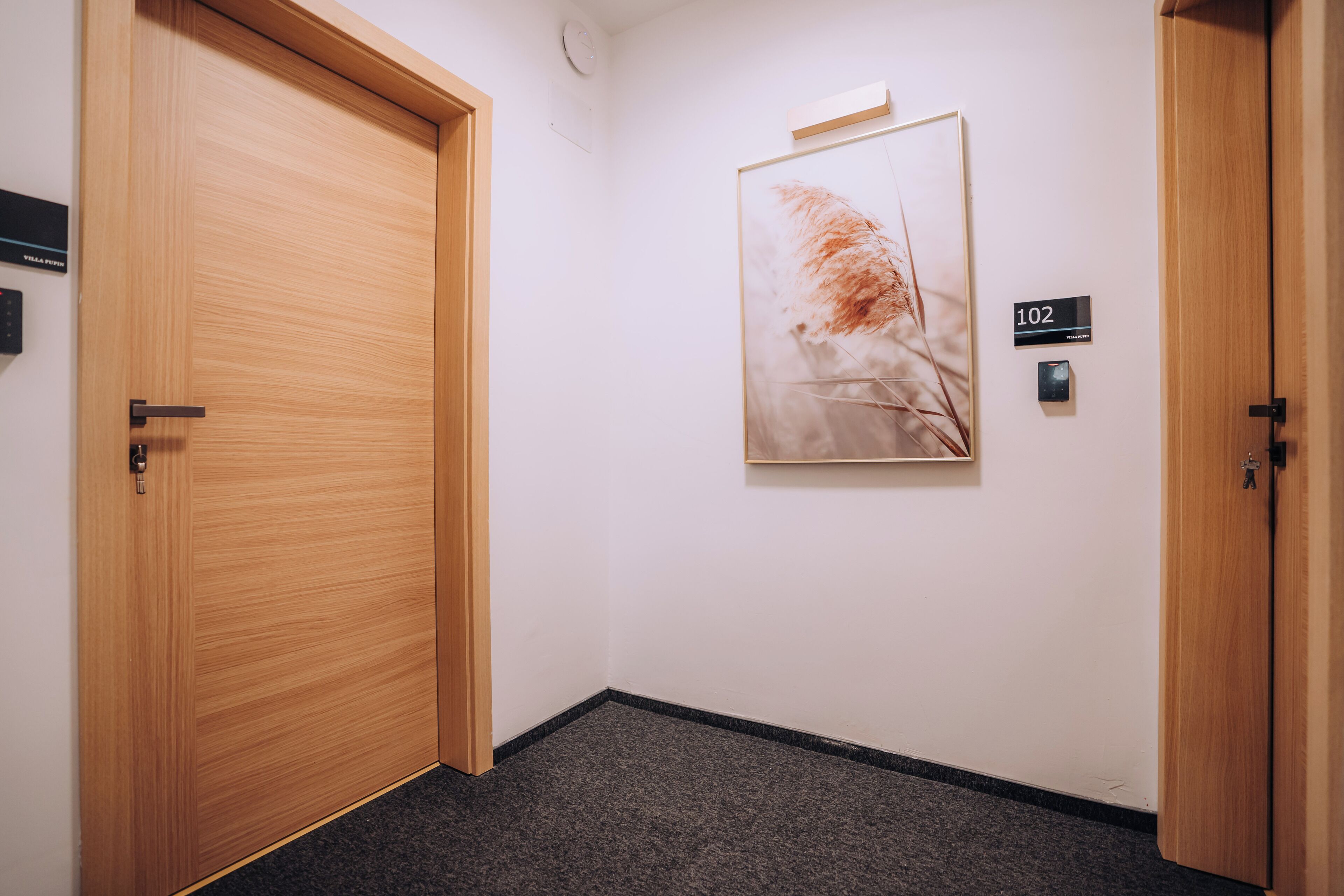 A hallway with wooden doors, a framed artwork on the wall, and a room number sign.