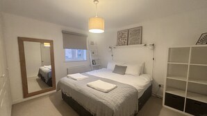 Een slaapkamer met een bed, nachtkastje, spiegel, raam en een inbouwkast.