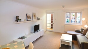 Een moderne woonkamer met een flatscreen televisie, een bank, een salontafel en een boekenkast met ingelijste foto's.