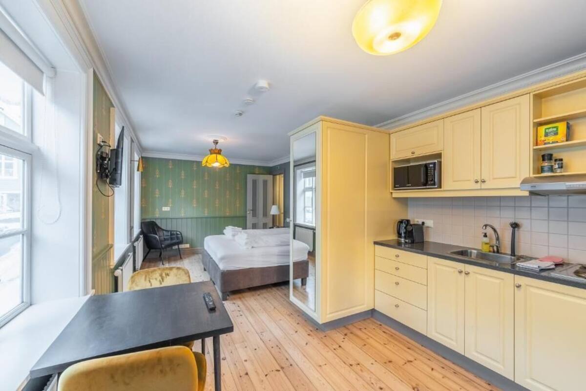 A compact hotel room with a bed, a small table, a chair, a kitchenette, and a window.