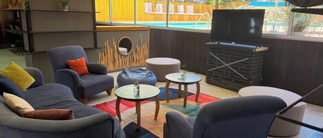 Una sala de estar moderna con vista a la piscina, que incluye asientos, un televisor y una pared de madera.