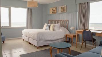Een slaapkamer met een bed, een bureau, een stoel en uitzicht op zee.