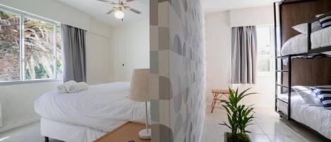 Una habitación de hotel moderna con una cama individual, un escritorio, un ventilador de techo y un ventanal grande.