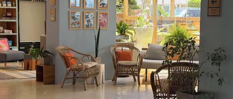 A spacious room with wicker furniture, a bookshelf, and a large window with a view of the outside.