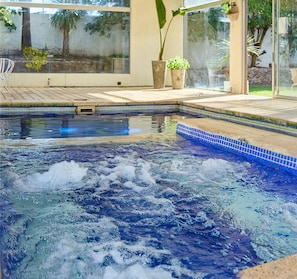 A hot tub with a tiled edge, surrounded by a patio area with potted plants and a view of trees through a glass door. - ZAG Coliving (Punta del Este)