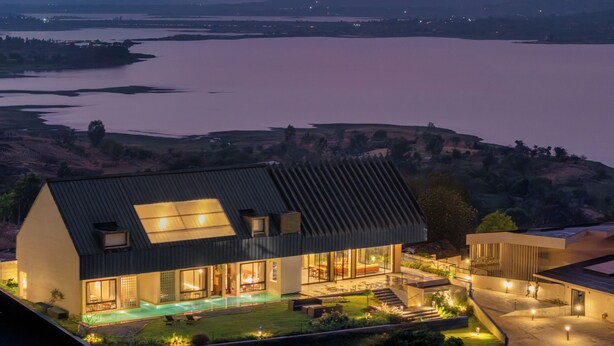 Una casa moderna con piscina, ventanas amplias y vistas a un lago y montañas.