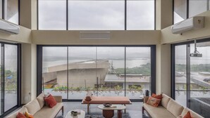 Una habitación amplia con techo alto, ventanas grandes, un conjunto de sofá, una mesa de centro y una silla.