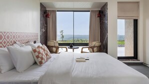 Habitación de hotel con una cama grande, dos sillas, una mesita y vistas al exterior.