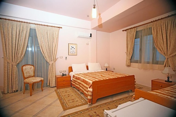 A bedroom with a bed, a chair, a nightstand, and a bedside table. - Hotel Primavera Vlore (Vlorë)