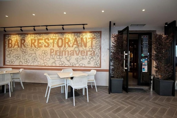 A restaurant interior with a large floral wall sign, white chairs, and a herringbone floor pattern. - Hotel Primavera Vlore (Vlorë)