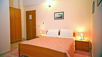 A bedroom with a bed, two bedside tables with lamps, a wooden wardrobe, and a framed picture on the wall.