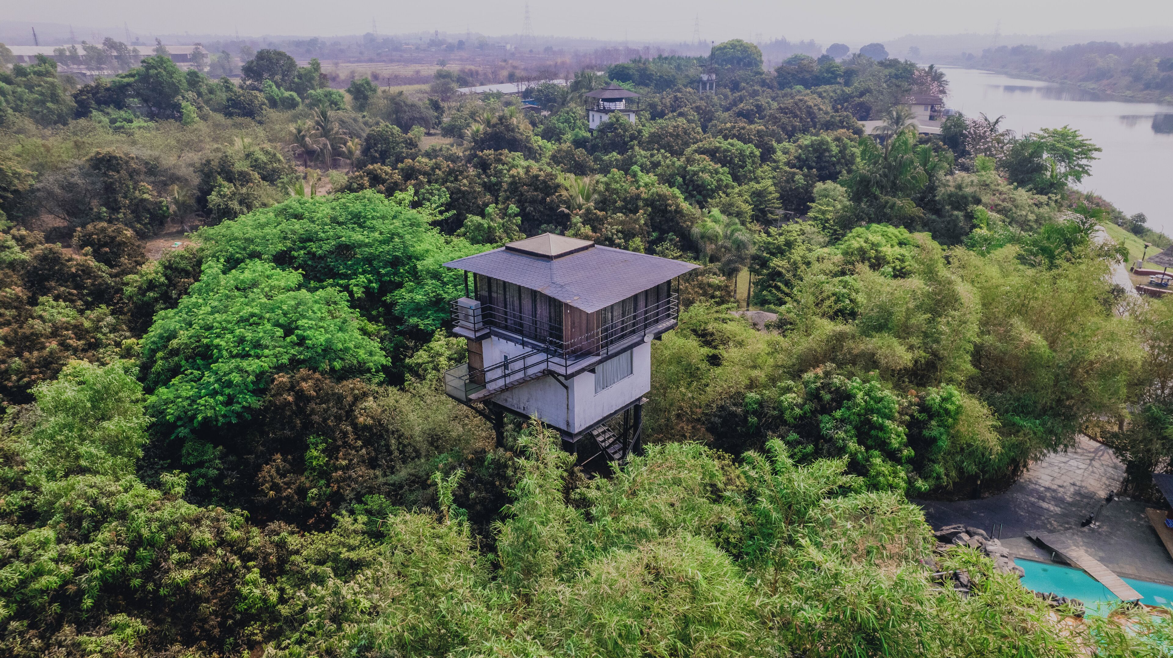 A high-rise tower with a flat roof, surrounded by dense greenery and a lake in the background.