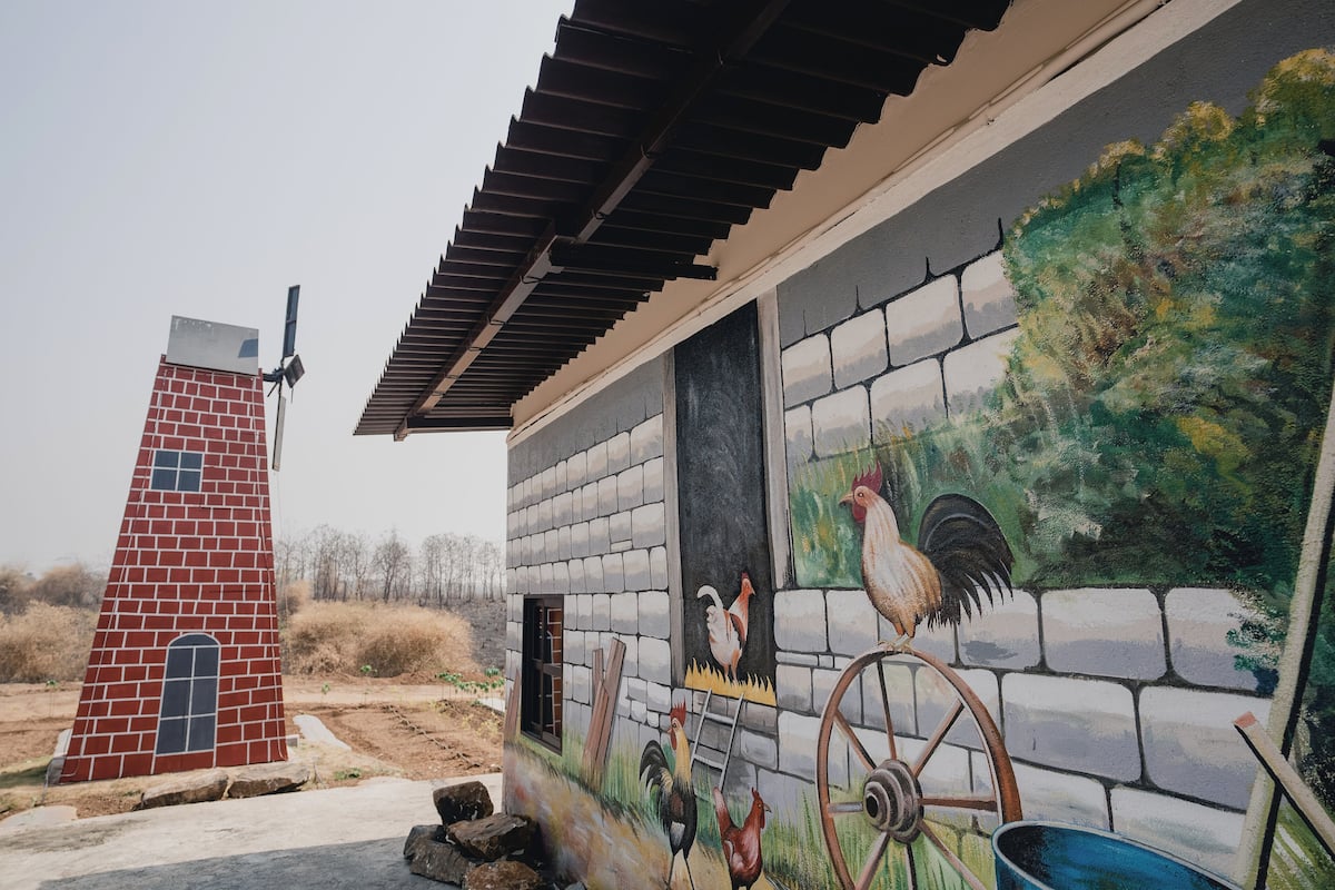 A building with a mural of roosters and a rooster on a wheel, a brick chimney, and a metal roof.