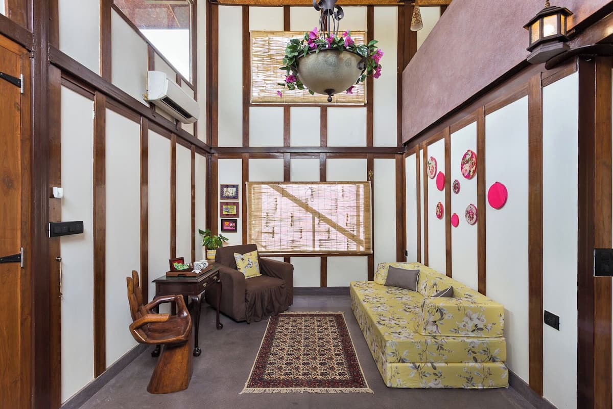 A traditional Japanese-style room with tatami flooring, a low wooden ceiling, a hanging flower pot, a futon sofa, a small wooden table, and a shoji screen.