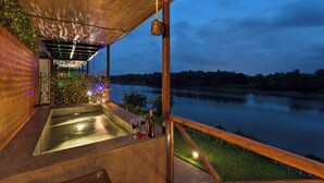 A modern outdoor hot tub area with a view of a lake at dusk. - Anchaviyo By Zuper (Vada)