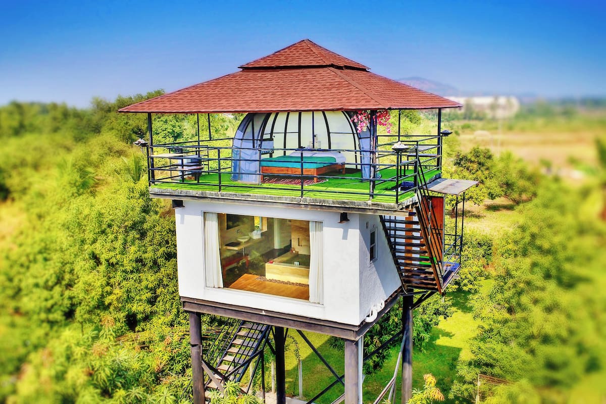 A treehouse with a red roof, a glass enclosure, and a wooden deck.