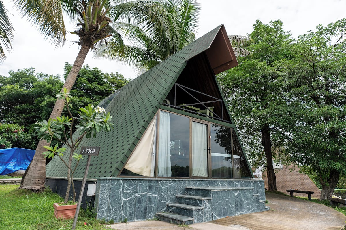 A small, modern house with a sloped roof, a balcony, and a staircase leading to the entrance.