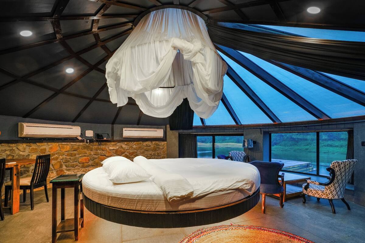 A bedroom with a hanging canopy bed, stone wall, and a view of the outdoors.
