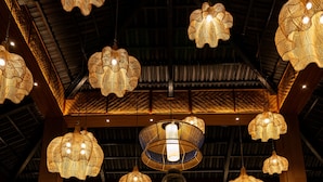 A large Buddha statue in a dimly lit room with multiple hanging lamps and a staircase leading to an upper level. - Anchaviyo By Zuper (Vada)