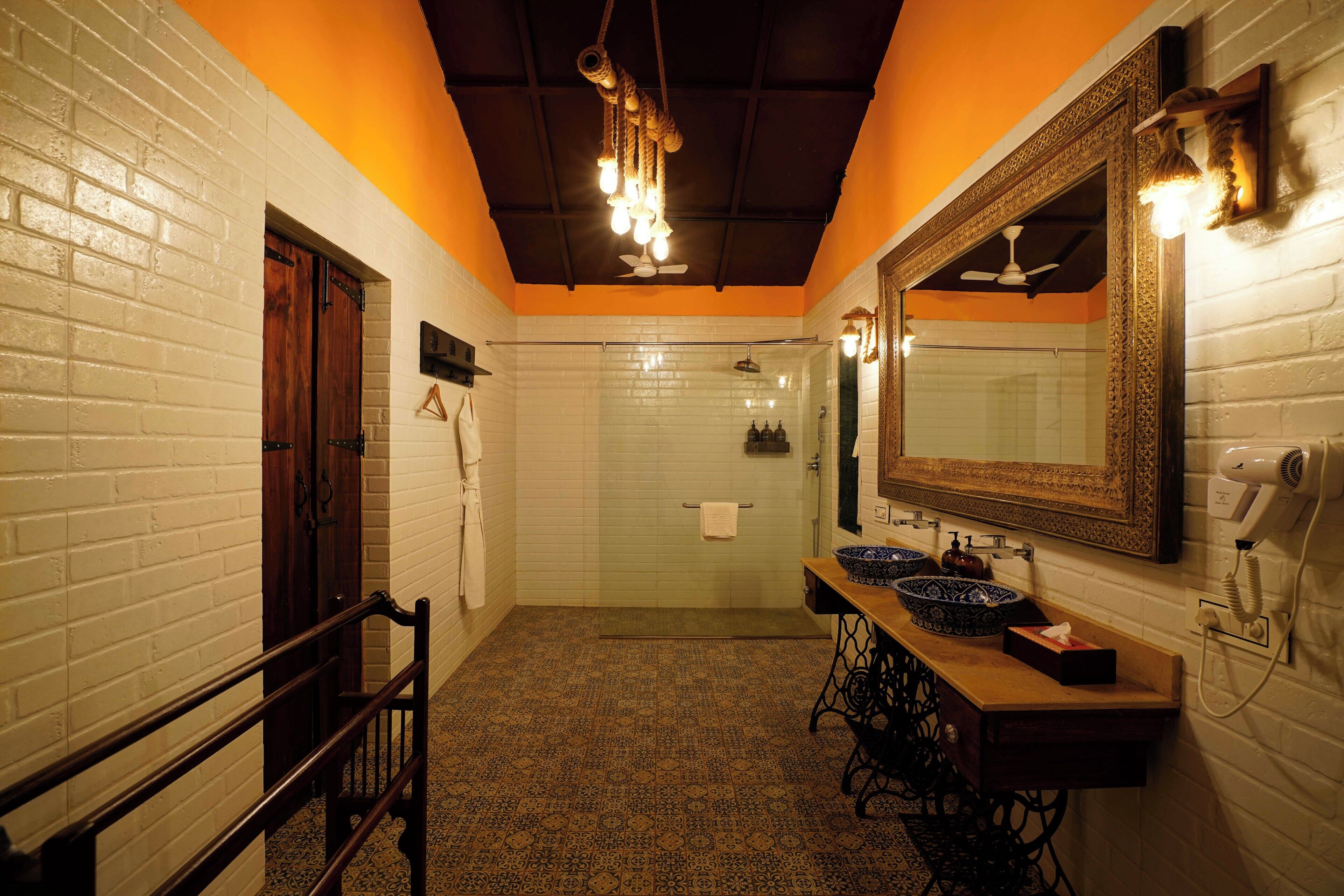 A bathroom with a white brick wall, a wooden door, a shower, a sink with a mirror, and a ceiling fan.