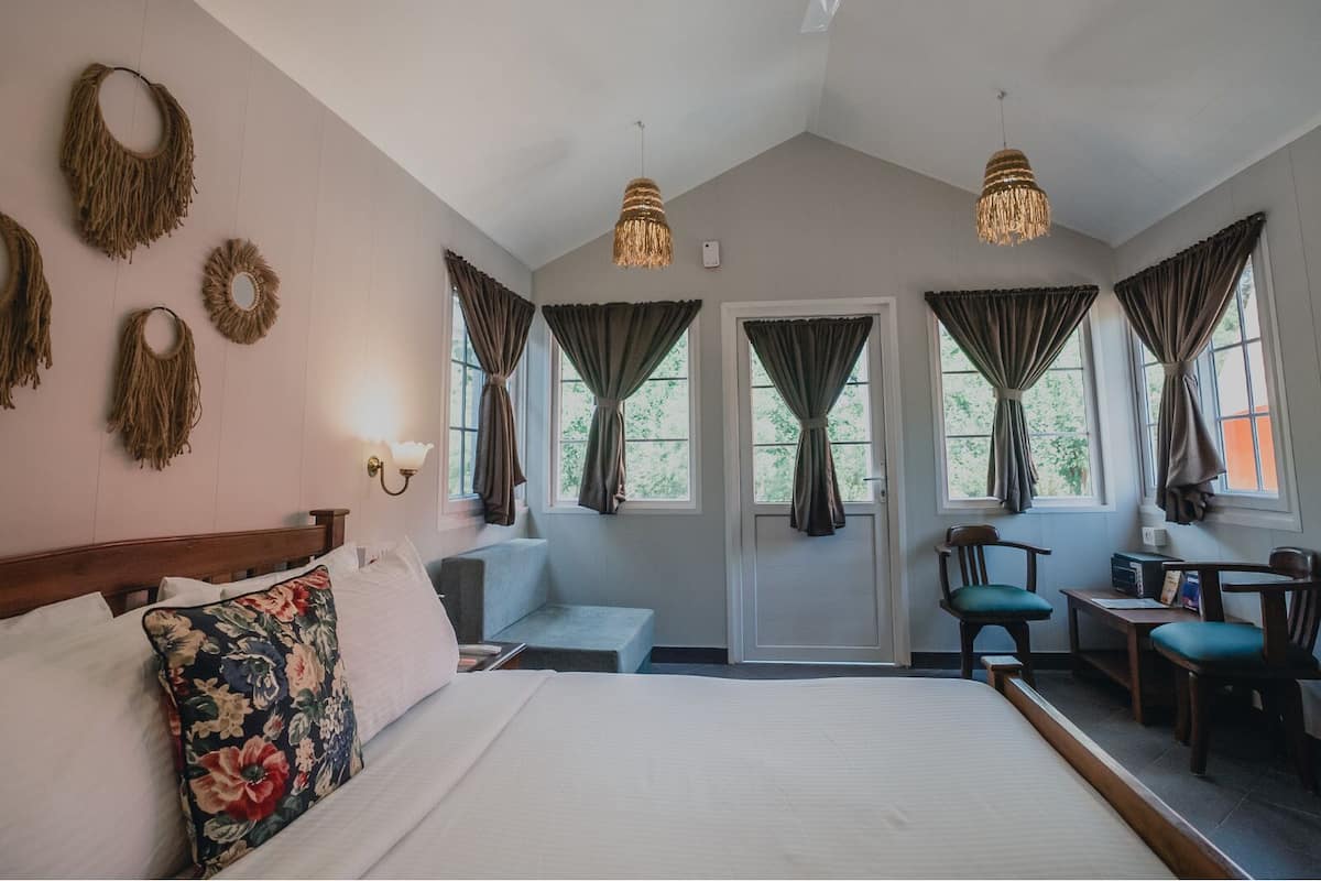 A bedroom with a large bed, a desk, two chairs, and a ceiling fan.
