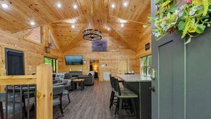 A wooden cabin interior with a dining area, kitchen, and seating space.