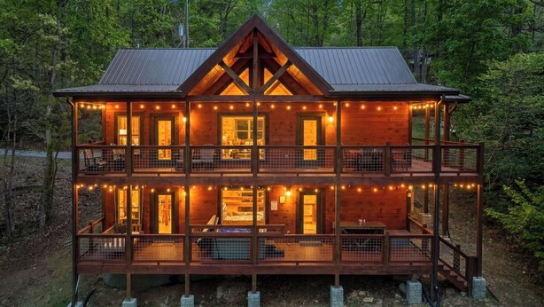 A two-story wooden cabin with a balcony, string lights, and a metal roof.