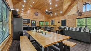 A wooden cabin interior with a dining area, kitchen, and seating space.