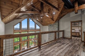 Um quarto espaçoso no estilo loft, com pé direito alto, grandes janelas, lareira de pedra e varanda com vista para o exterior.