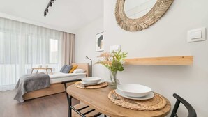 Ein modernes Hotelzimmer mit Bett, Esstisch mit Tellern, Blumen in einer Vase und einem gewebten Spiegel an der Wand.